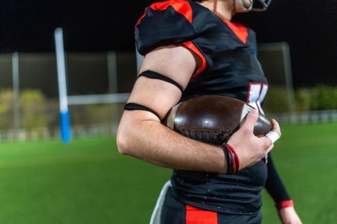 American football player preparing for a game, holding a ball firmly on a sports field lit by