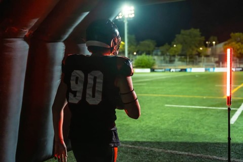 American football player in jersey number 90 emerges from an inflatable tunnel onto a floodlit