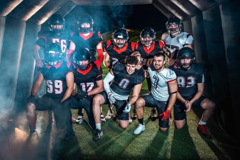 American football team poses united in helmets and pads, emerging from a smoky stadium tunnel under
