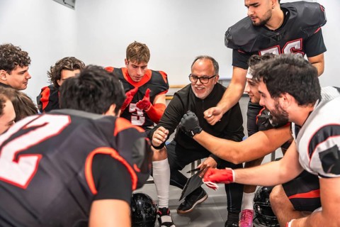 American football coach delivering a motivational speech to a diverse team of young players in