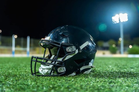 American football helmet lying on green artificial turf field with goal posts and bright stadium