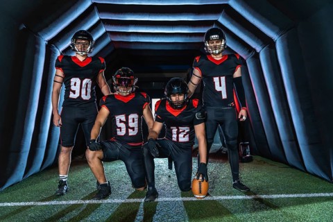 American football players in black and red uniforms, some kneeling and some standing in a dark