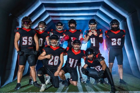 American football team players in uniforms and helmets posing together inside a stadium inflatable
