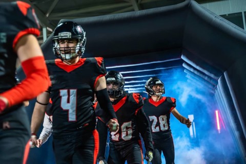 American football players, wearing black and red uniforms with helmets, walking into the stadium