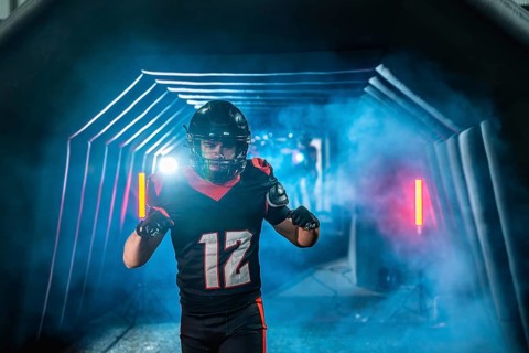 American football player with helmet and uniform running from a smoky tunnel with blue and red
