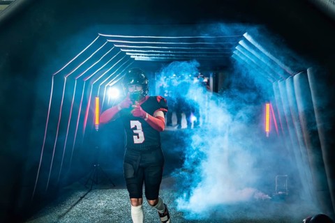 American football player in uniform and helmet emerging from a stadium tunnel filled with smoke and