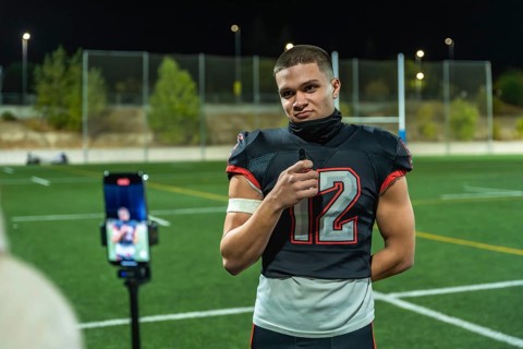 American football player in uniform number 12, standing on a green sports field at night, holding a