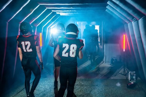 American football players wearing jerseys and helmets, emerging from a dark tunnel towards a bright