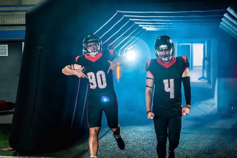 American football players in black and red uniforms and helmets are making an entrance, emerging