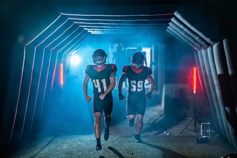 American football players burst from a smoky stadium tunnel in helmets and jerseys, running onto