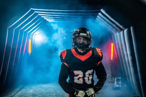 American football player in uniform and helmet emerges from a fog filled stadium tunnel into