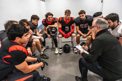 American football coach explaining game strategy to his young diverse football team members, who