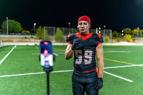 Football player in uniform recording video on a smartphone with a lavalier microphone, creating new