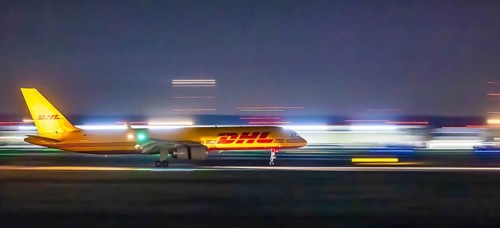 Stuttgart Airport in the early morning. DHL cargo plane landing. Light traces with motion blur.