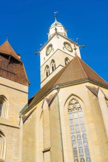Gothic church tower with striking clock and pointed roofs in front of a bright blue sky, St