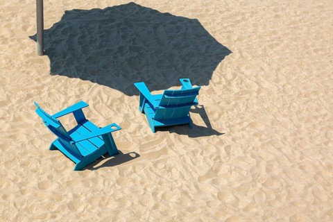 Teal blue wooden Adirondack chairs and casted shadow from parasol in fine tan sand, Clock Tower