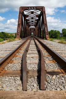 Railroad tracks leading to old rusted Terrebonne Pratt truss railroad bridge over Des Mille-Iles
