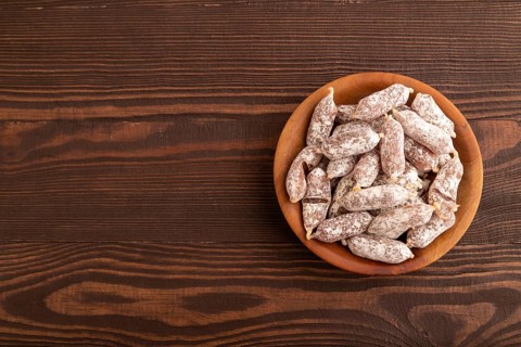Small smoked Chicken sausages in wooden bowl on brown wooden background. top view, flat lay, copy