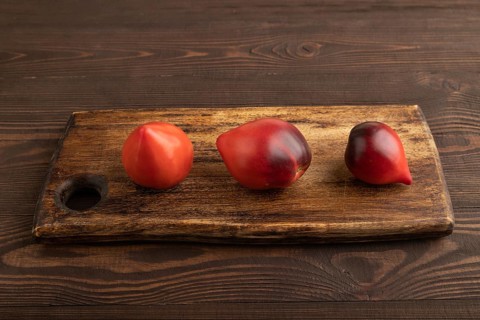 Red Heart shape tomatoes on cutting board on brown wooden background. Side view, copy space.