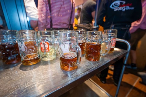 Row of beer mugs on a long wooden table at a festive event with people in the background,