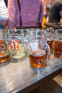 Large glass mugs of beer on a wooden table surface in a lively festival setting, Cannstatter Wasen