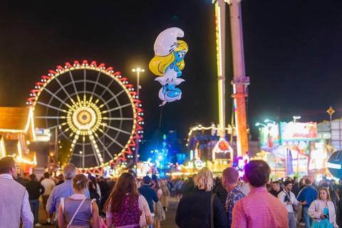 People enjoying the hustle and bustle of a fairground at night with a large Ferris wheel in the