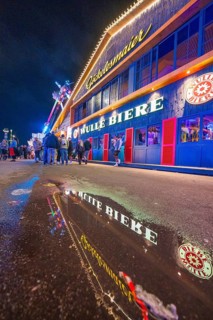 Reflection of the colourful lights of a beer hall on a wet street at night, Cannstatter Wasen folk