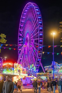 A large, colourfully illuminated Ferris wheel dominates the night-time scenery of a lively