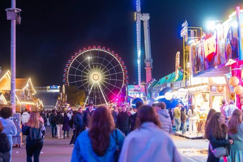 Lively funfair at night with lots of people and a large, illuminated Ferris wheel, Cannstatter