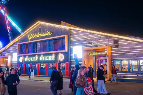Illuminated building at night at the funfair with people passing by, Cannstatter Wasen funfair,