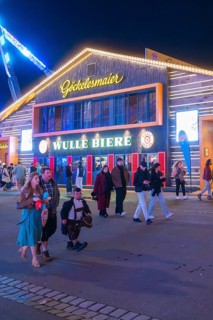 People strolling at night in front of an illuminated building at the funfair, Cannstatter Wasen