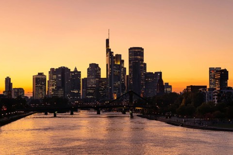 The evening sky behind the Frankfurt banking skyline glows orange and yellow shortly after sunset,