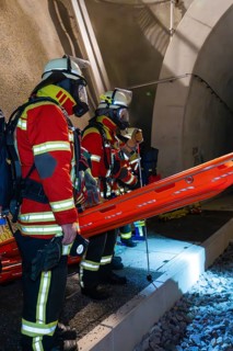 Firefighters in protective clothing stand ready at the tunnel entrance at night, firefighting