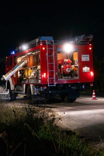 Fire engine at night with open back, illuminated by lanterns and blue lights, fire brigade exercise