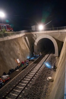 Rescue workers working in an illuminated tunnel at night, railway tracks in the foreground, fire