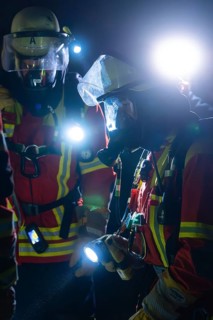 Two firefighters in protective clothing and breathing masks with torches in action at night, fire
