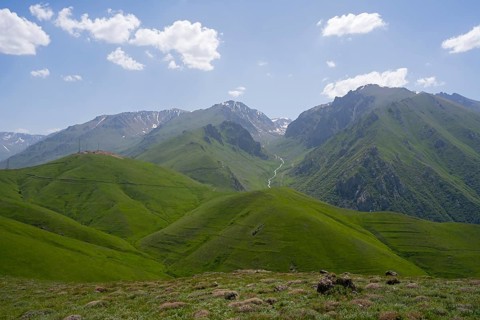 Green hills in front of mountains with clouds in the blue sky, at the highest pass of Armenia,