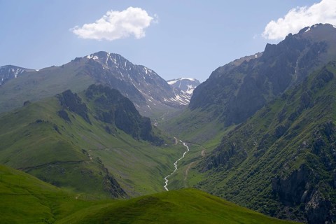 Mountain landscape with green valleys and a small river under a clear sky and clouds, at the