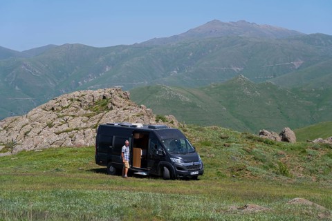Man next to a camper in a green, mountainous landscape, camper at the highest pass of Armenia,