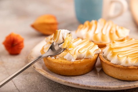 French lemon tart with meringue on brown concrete background, cup of coffee, orange linen textile,