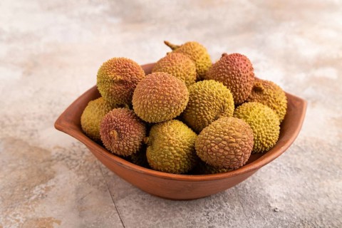 Ripe Lychee on clay bowl on brown concrete background, side view, close up, minimalism