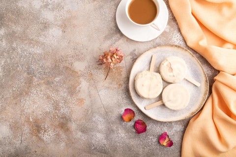 ?hocolate Ice cream in white glaze, cup of coffee, on brown concrete background and orange textile,
