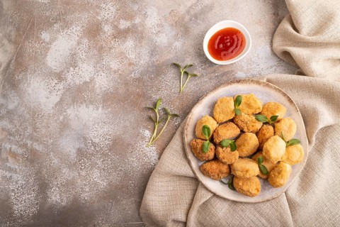 Fried crispy Chicken Nuggets with ketchup, microgreen on brown concrete background and linen