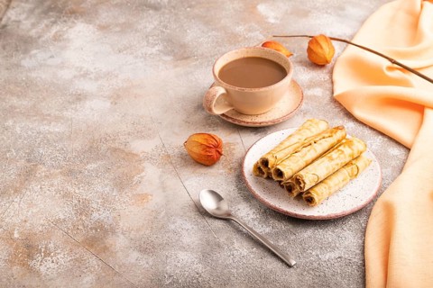 Waffles with caramel on brown concrete background and orange linen textile, cup of coffee, side