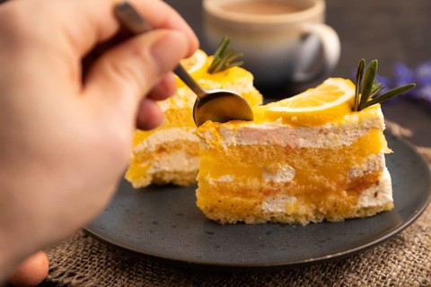 Lemon cake with hand on black concrete background and linen textile, cup of coffee, side view,