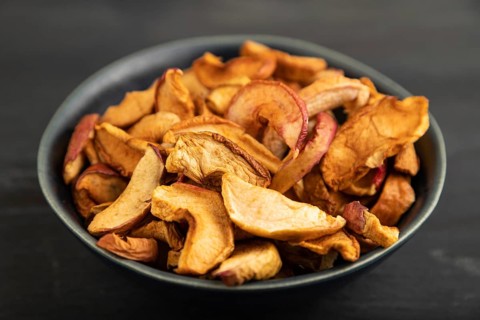 Dried Apples in ceramic bowl on black wooden background. Side view, close up. healthy food,