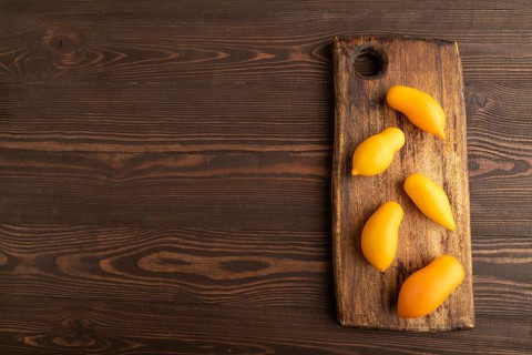 Yellow tomatoes on cutting board on brown wooden background. Top view, copy space, flat lay.
