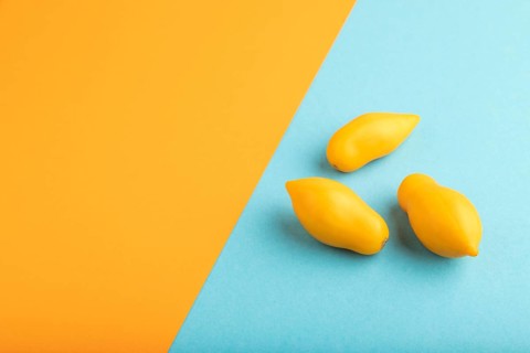 Yellow tomatoes on blue and orange pastel paper background. Side view, copy space. healthy food,