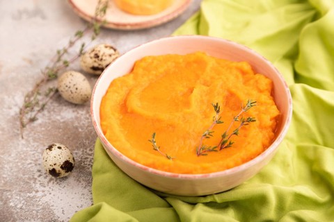 Sweet potato porridge in ceramic bowl on brown concrete background and green textile. Diet, healthy