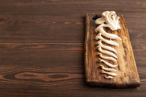 Raw Oyster mushroom, Pleurotus ostreatus on cutting board on brown wooden background. Side view,